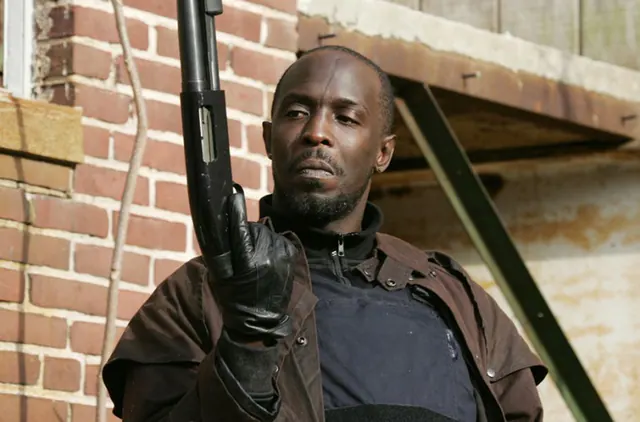 Omar holding a shotgun against a brick exterior in The Wire.